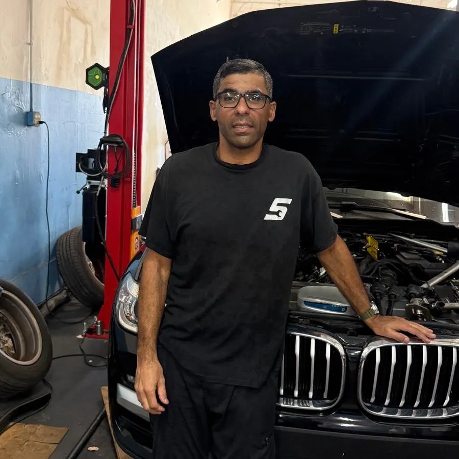 Sandro, dono e mecânico, ao lado de uma BMW de capô aberto na Phil's Electric Auto Expert