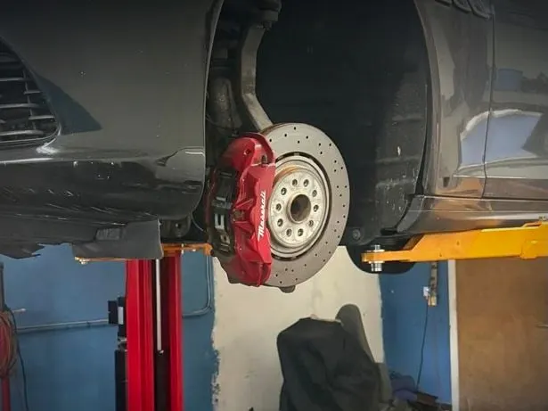 Brake disc and red caliper exposed during brake service at Phil's Electric Auto Expert in Pompano Beach